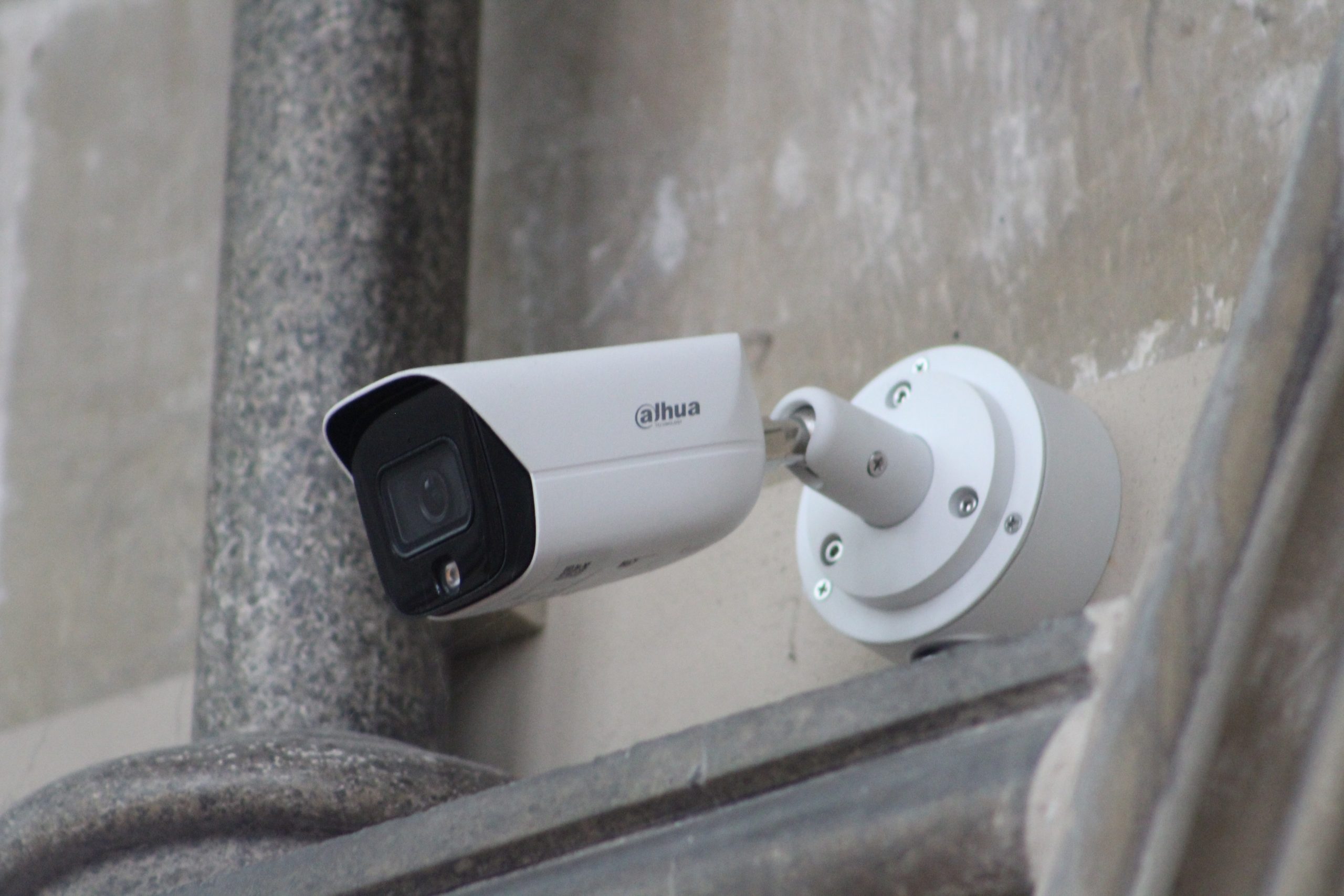 Wall mounted bullet style CCTV security camera installed on an exterior wall, featuring a white housing, visible lens, and mounting bracket.