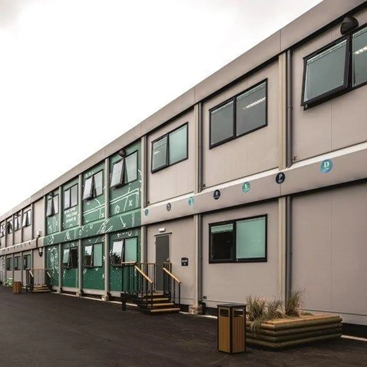 Exterior view of a modern two storey commercial building with rows of windows, signage along the facade, and a paved walkway leading to the entrances.