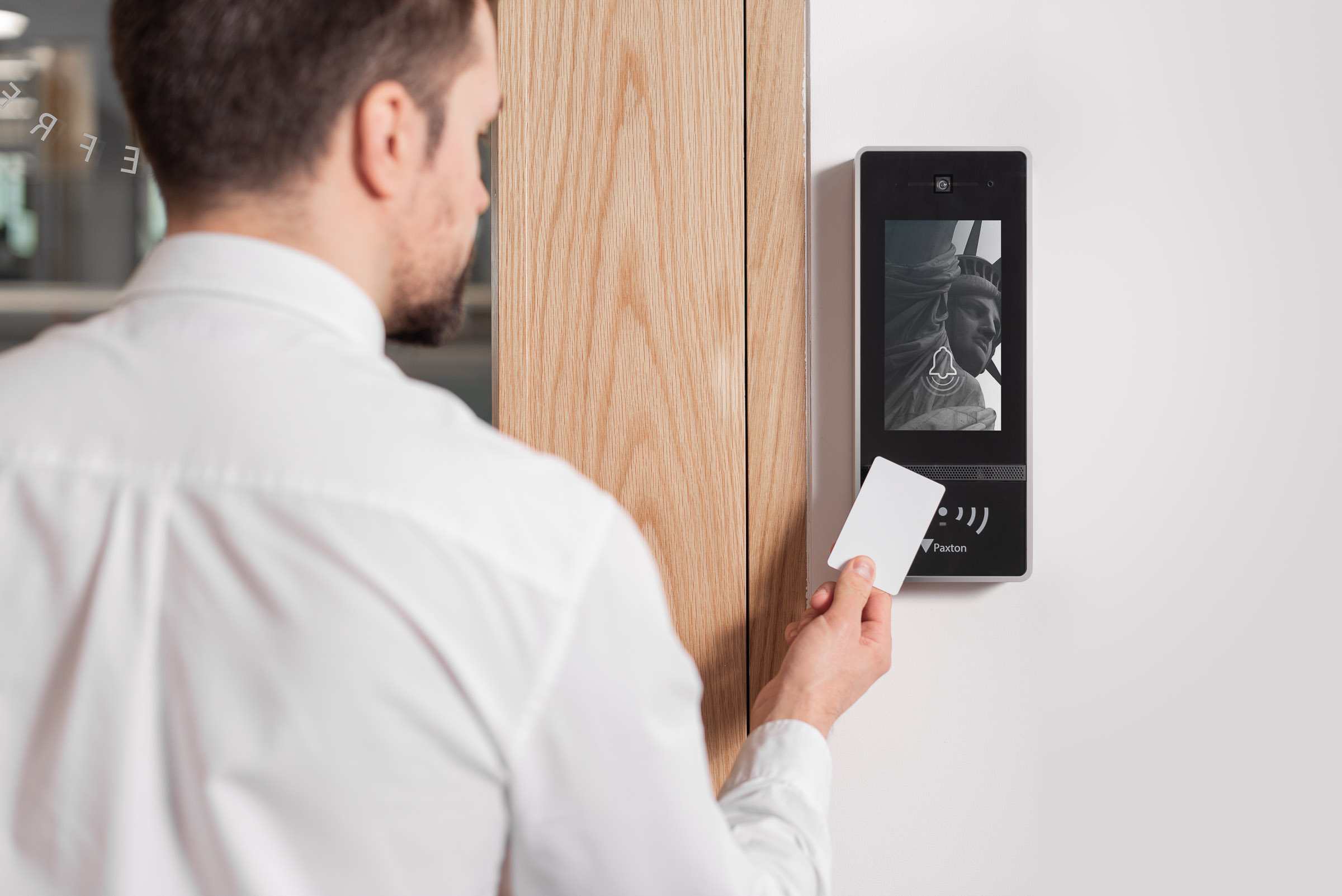 Person holding a contactless access card near a wall mounted video intercom and access control panel beside a wooden door.