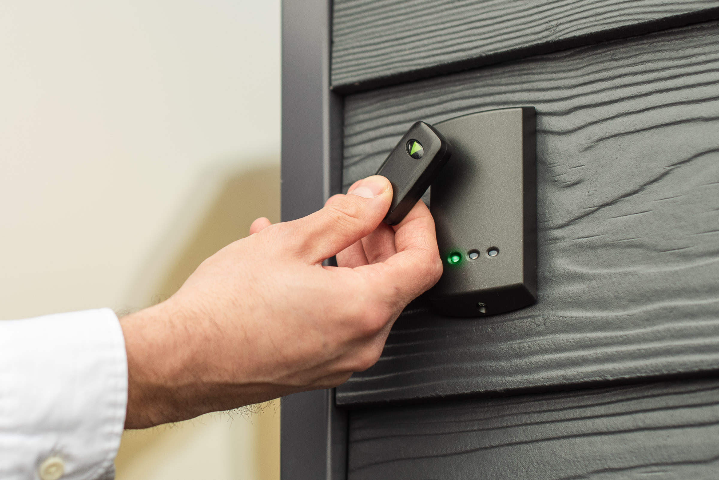Close up of a hand holding an access control key fob near a wall mounted reader, with indicator lights visible on the device.