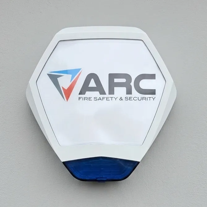 External alarm sounder mounted on a wall, featuring ARC Fire Safety and Security branding on a white casing with a blue strobe light at the base.