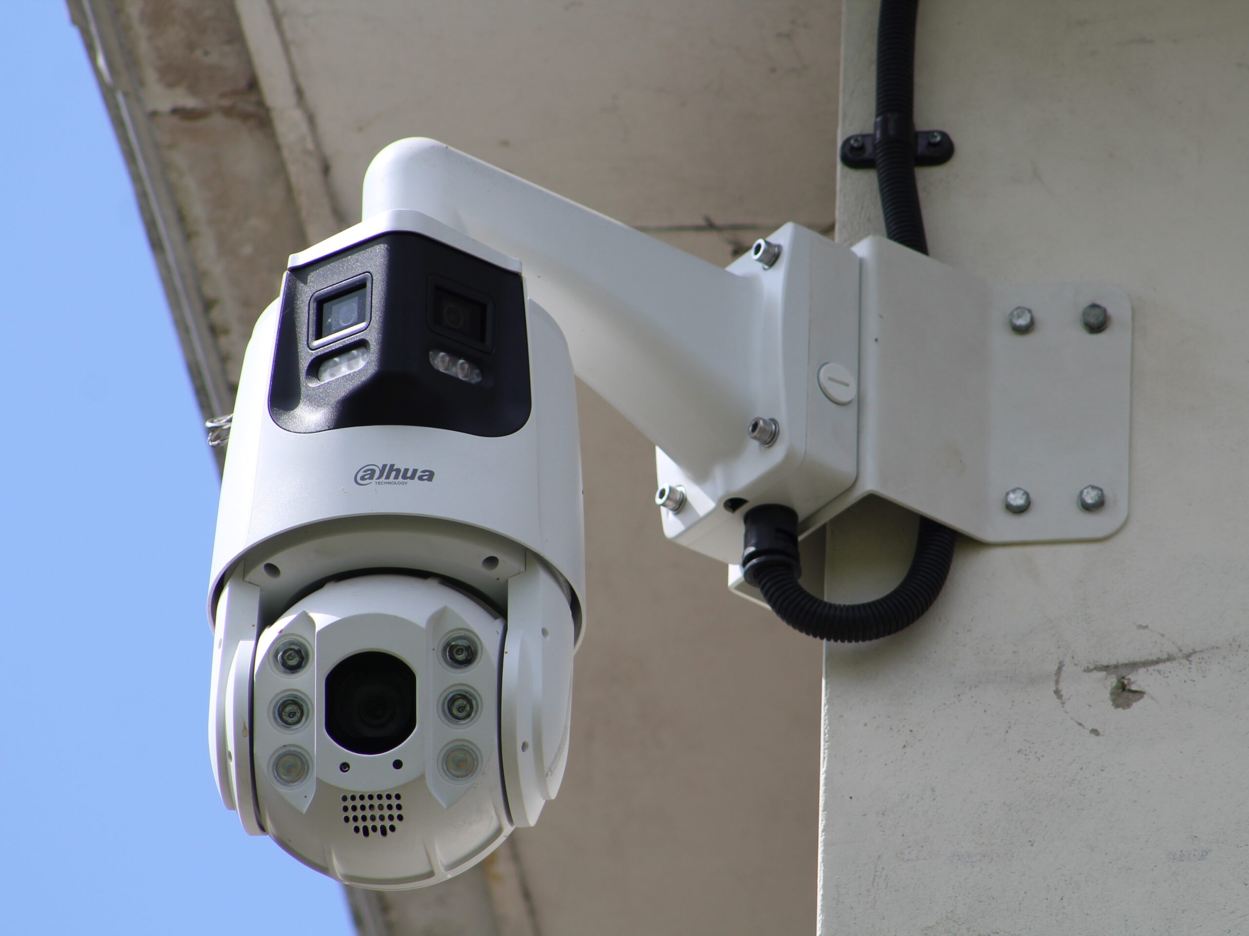 Wall mounted CCTV security camera installed on the exterior of a building, attached to a white mounting bracket with visible cabling.